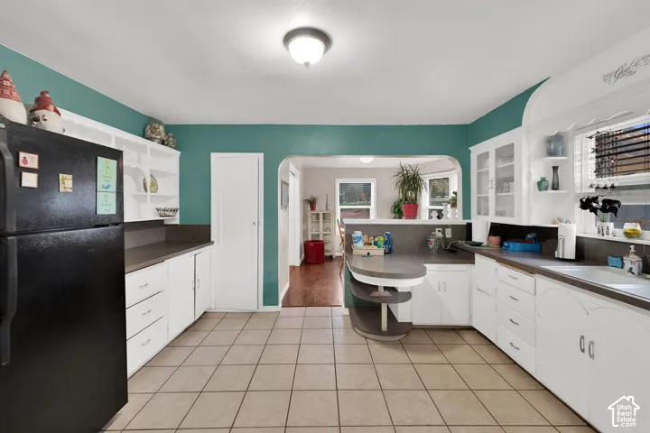 Kitchen featuring white shaker-style cabinetry, dark solid-surface countertops, built-in display shelving, and neutral tile flooring