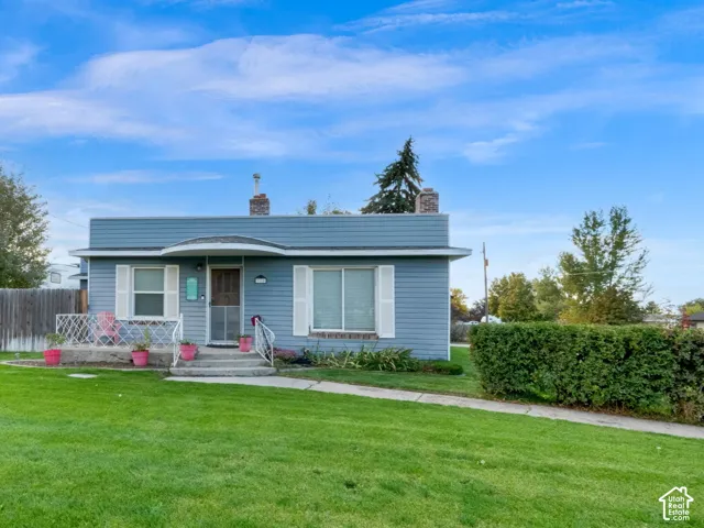 Single-story exterior featuring blue horizontal siding, a covered front porch with decorative metal railing, and a concrete walkway