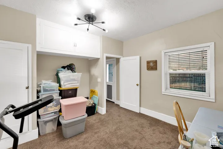 Multi-functional room featuring wall-to-wall carpeting, built-in overhead cabinetry, a multi-arm modern light fixture, and a window with horizontal blinds