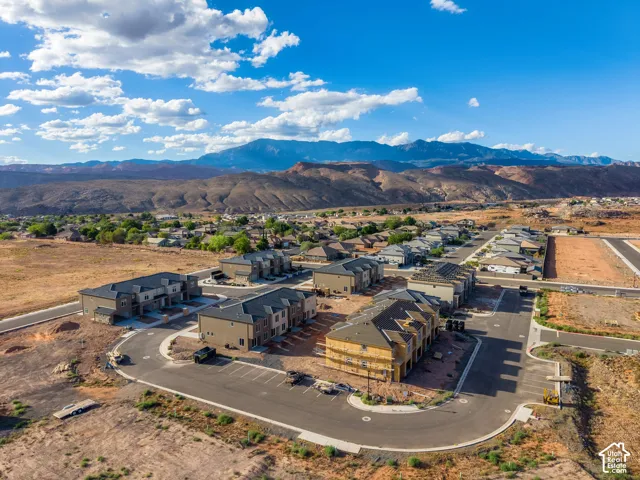 Multi-family residential community featuring multi-story structures with neutral-toned exteriors, asphalt shingle roofing, paved road infrastructure, and a mountainous horizon backdrop