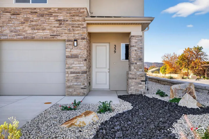 Exterior facade featuring stacked stone veneer, a covered entryway, a paneled front door, an attached garage, and xeriscaped front grounds