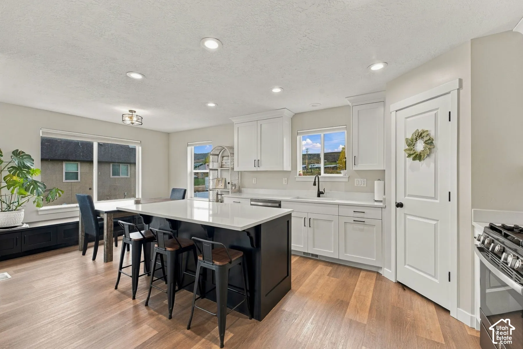 Kitchen featuring an expansive center island with quartz countertops, custom shaker-style cabinetry, matte black hardware, recessed lighting, and wood-finish flooring