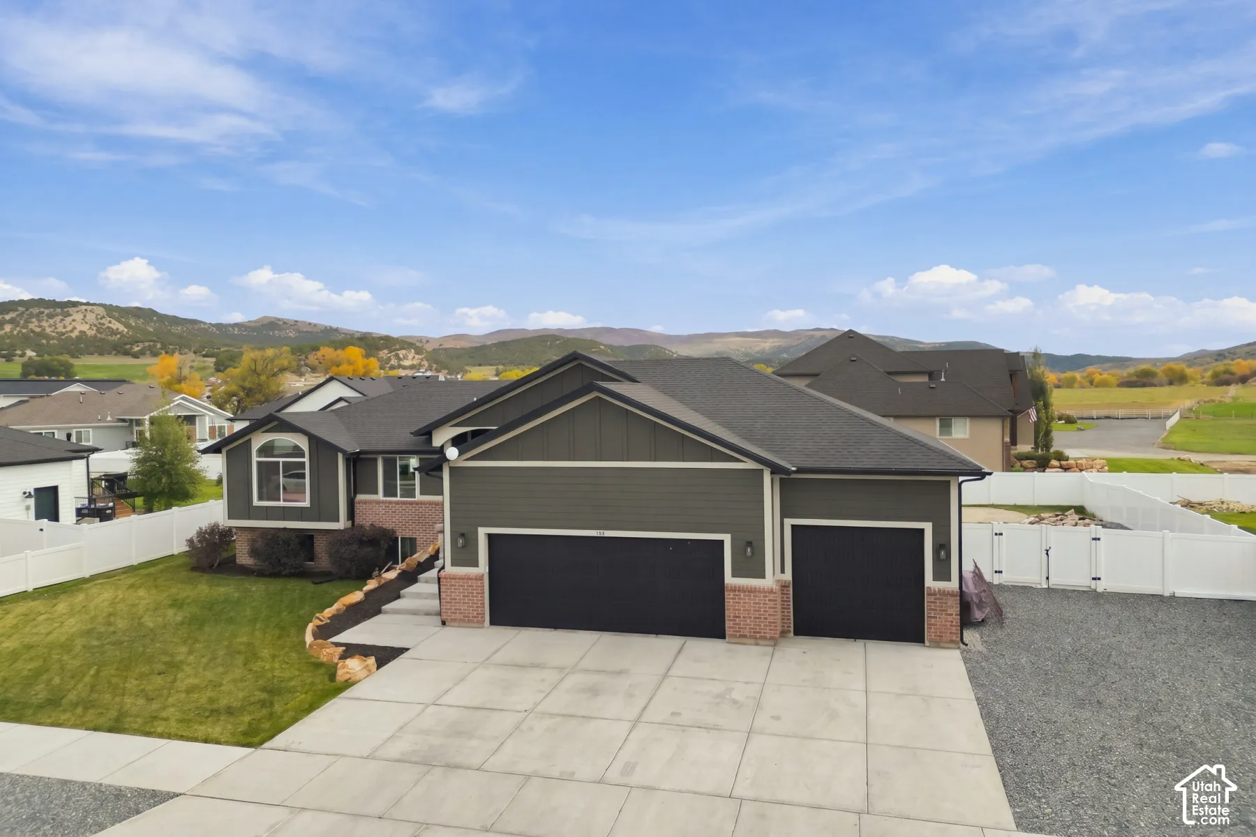 Exterior featuring a multi-gabled roofline, mixed brick and horizontal siding, a three-car garage, white vinyl perimeter fencing, and mountain scenery