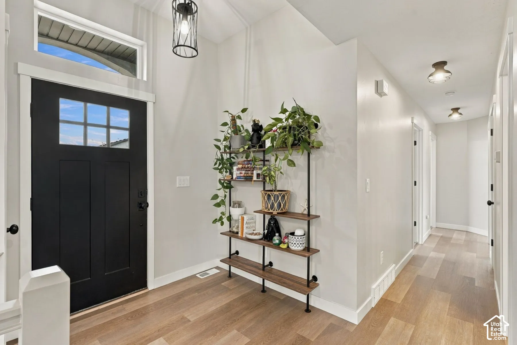 Entryway featuring a black-paneled front door with glass transom, high ceilings, wood-finish flooring, and industrial-style pendant lighting