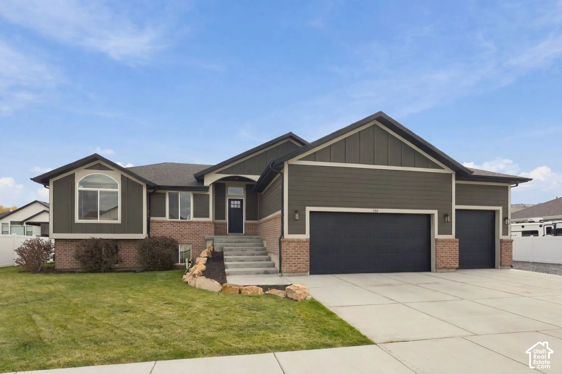 Exterior featuring vertical siding and brick masonry, three-car garage, concrete driveway, and stone landscaping accents