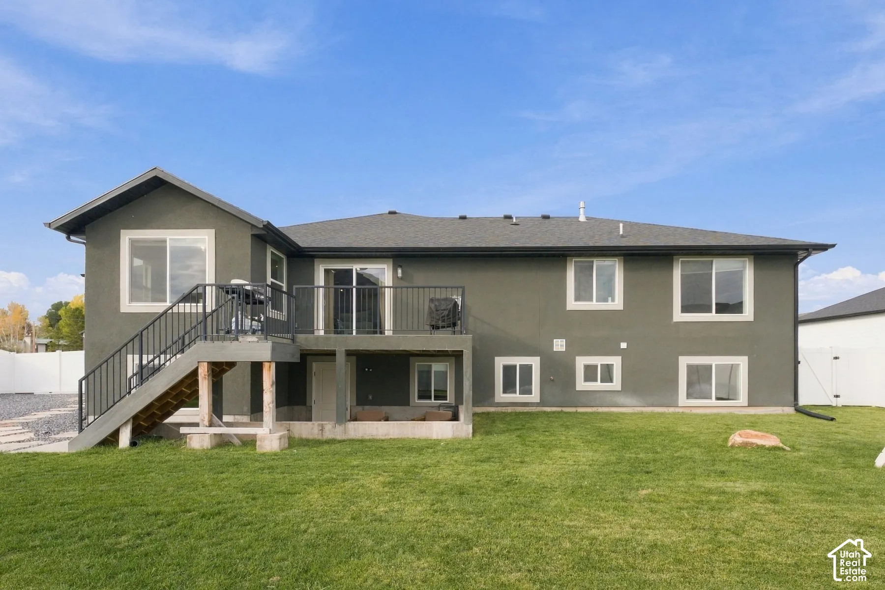 Rear exterior featuring a raised deck with metal railings, a staircase leading to the ground level, multi-pane windows, and an expansive grass lawn
