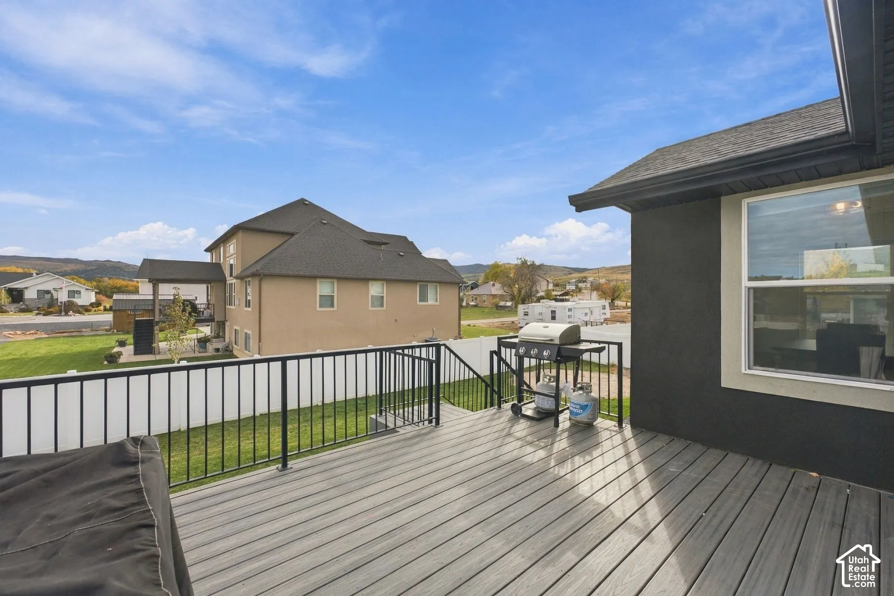 Elevated composite decking featuring black metal railing, stairs to the backyard, and white vinyl privacy fencing