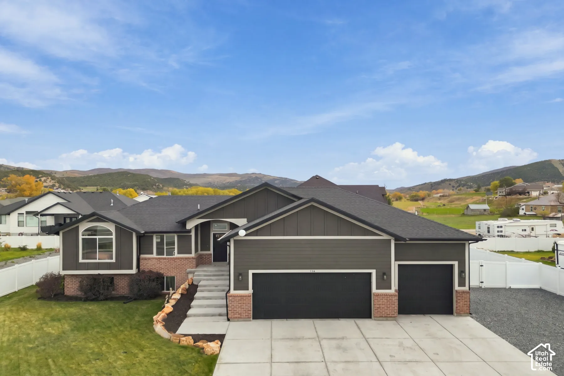 Single-level exterior featuring dark horizontal siding, brick accents, an attached three-car garage, concrete driveway, and mountain backdrop