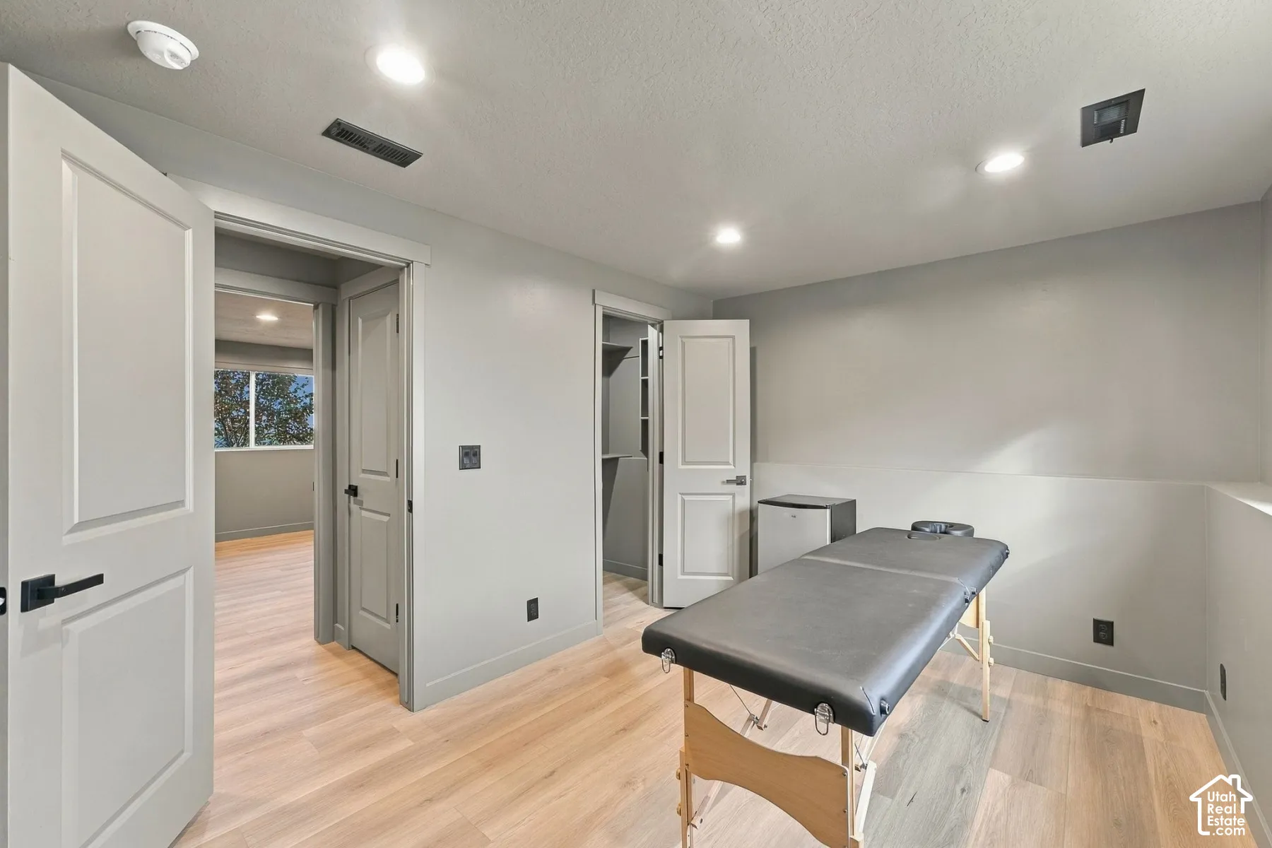 Interior room featuring wood-finish flooring, recessed lighting, neutral wall paint, solid-core doors with matte black hardware, and a walk-in closet with built-in shelving