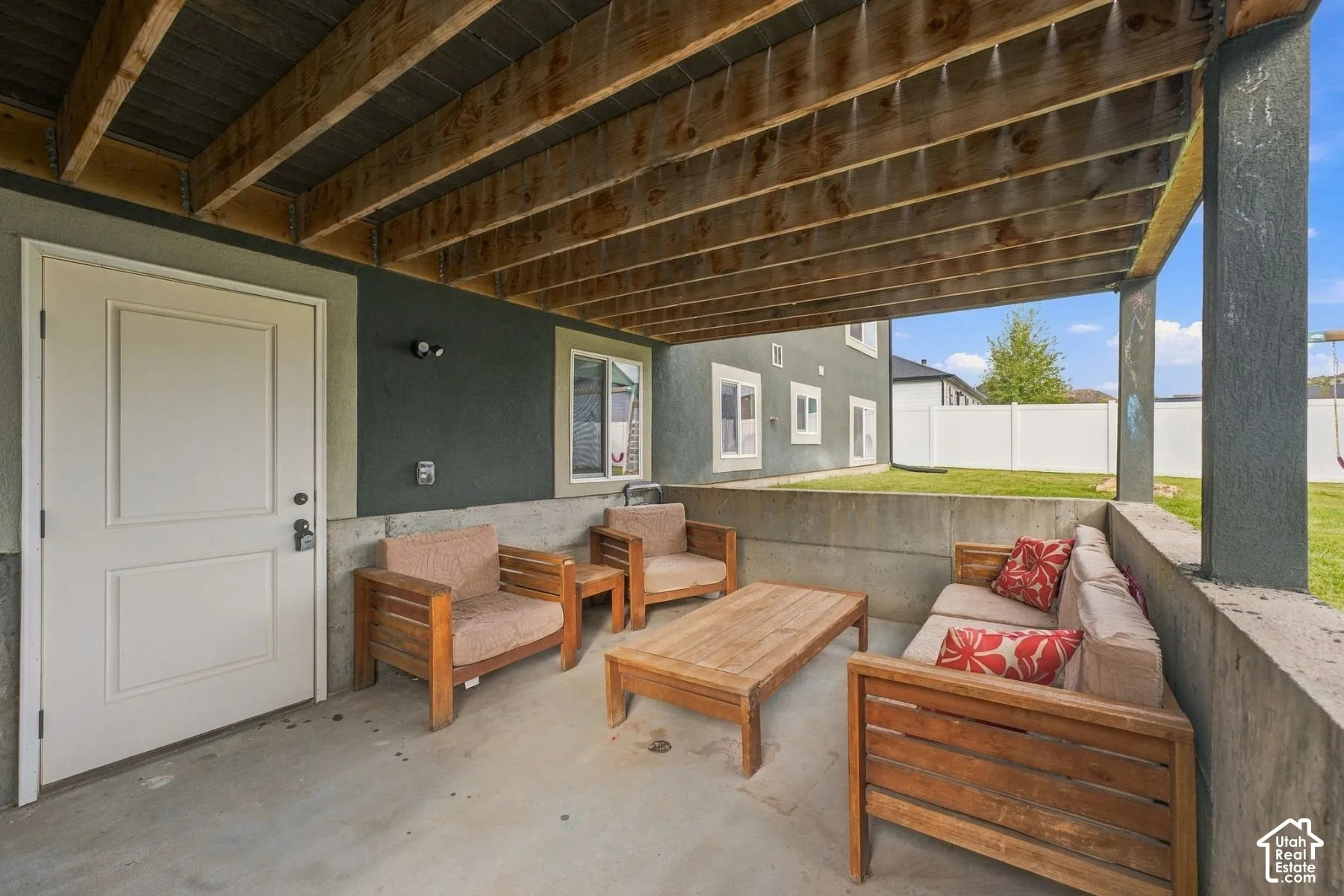 Covered patio featuring an exposed joist ceiling, concrete flooring, and a low-profile concrete retaining wall