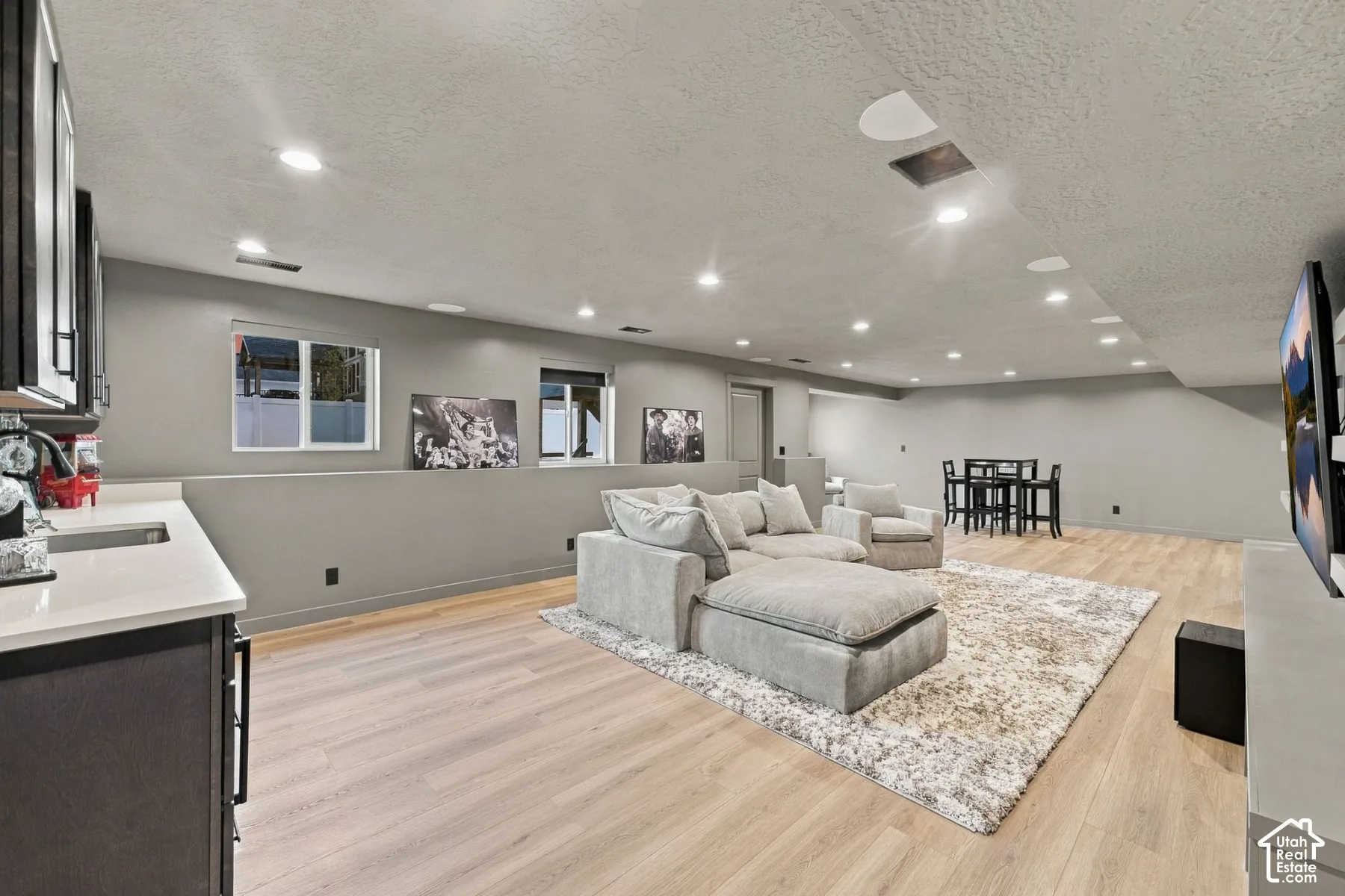 Open-concept recreation space featuring warm wood-finish flooring throughout, recessed ceiling lighting, neutral wall finishes with chair rail detail, and built-in shelving