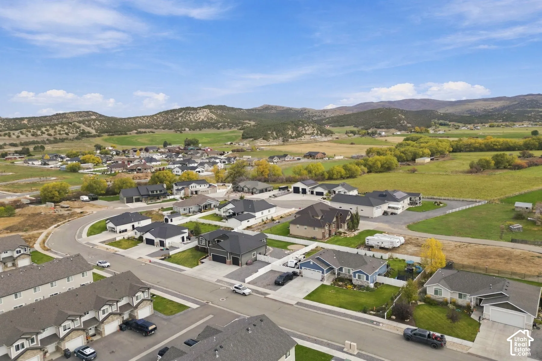 Aerial perspective featuring multi-level residential structures, concrete driveways, manicured lawns, and expansive mountain scenery