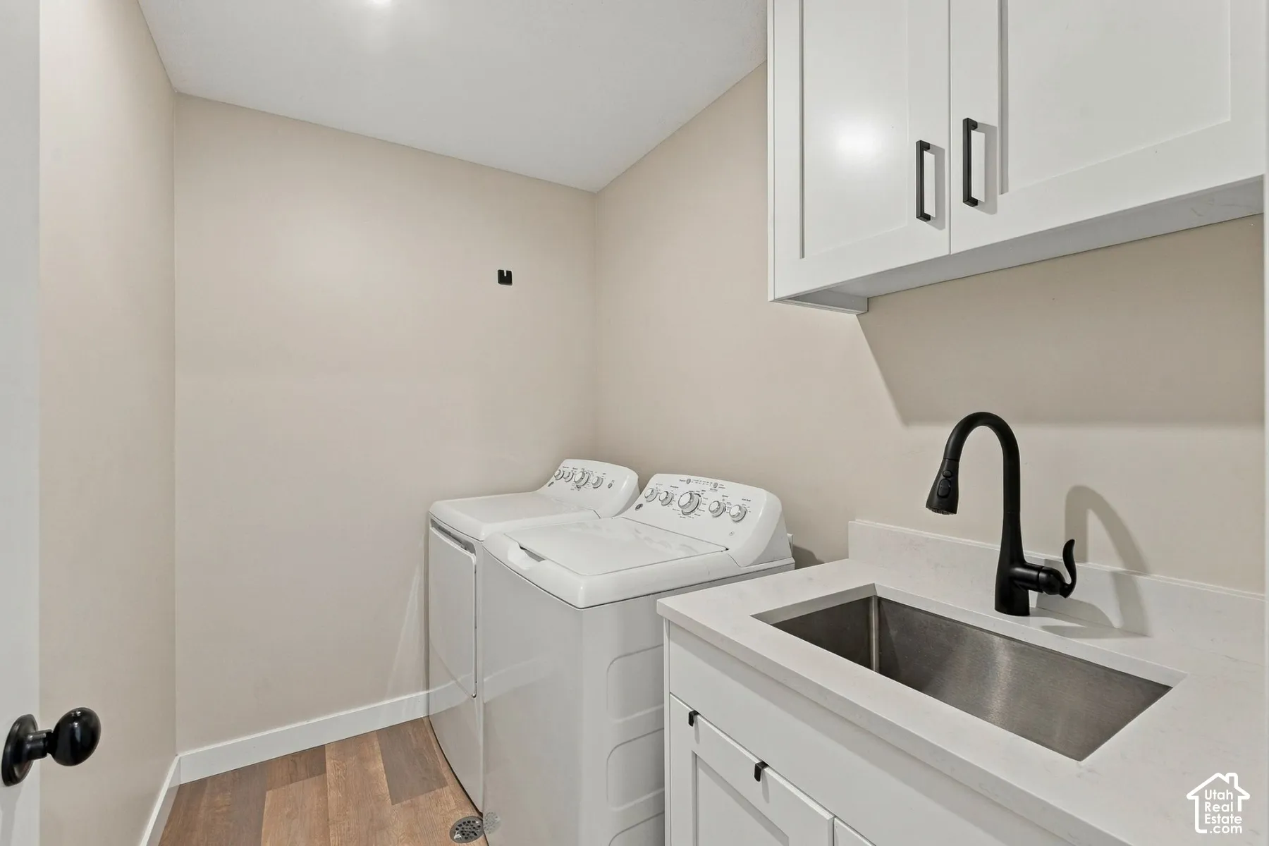 Utility room featuring white cabinetry, a stone-surfaced countertop with an integrated stainless steel sink, a matte black high-arch faucet, and wood-finish flooring