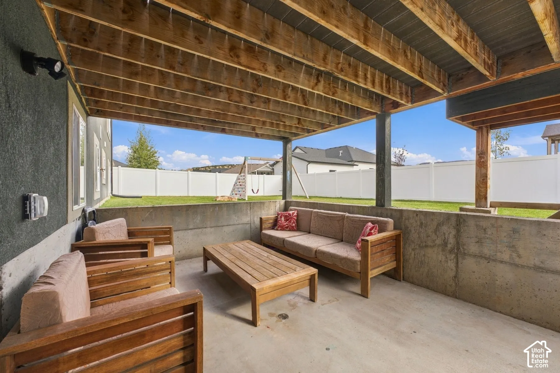 Covered patio featuring an exposed wood-beam ceiling, concrete foundation walls, and a fully fenced backyard
