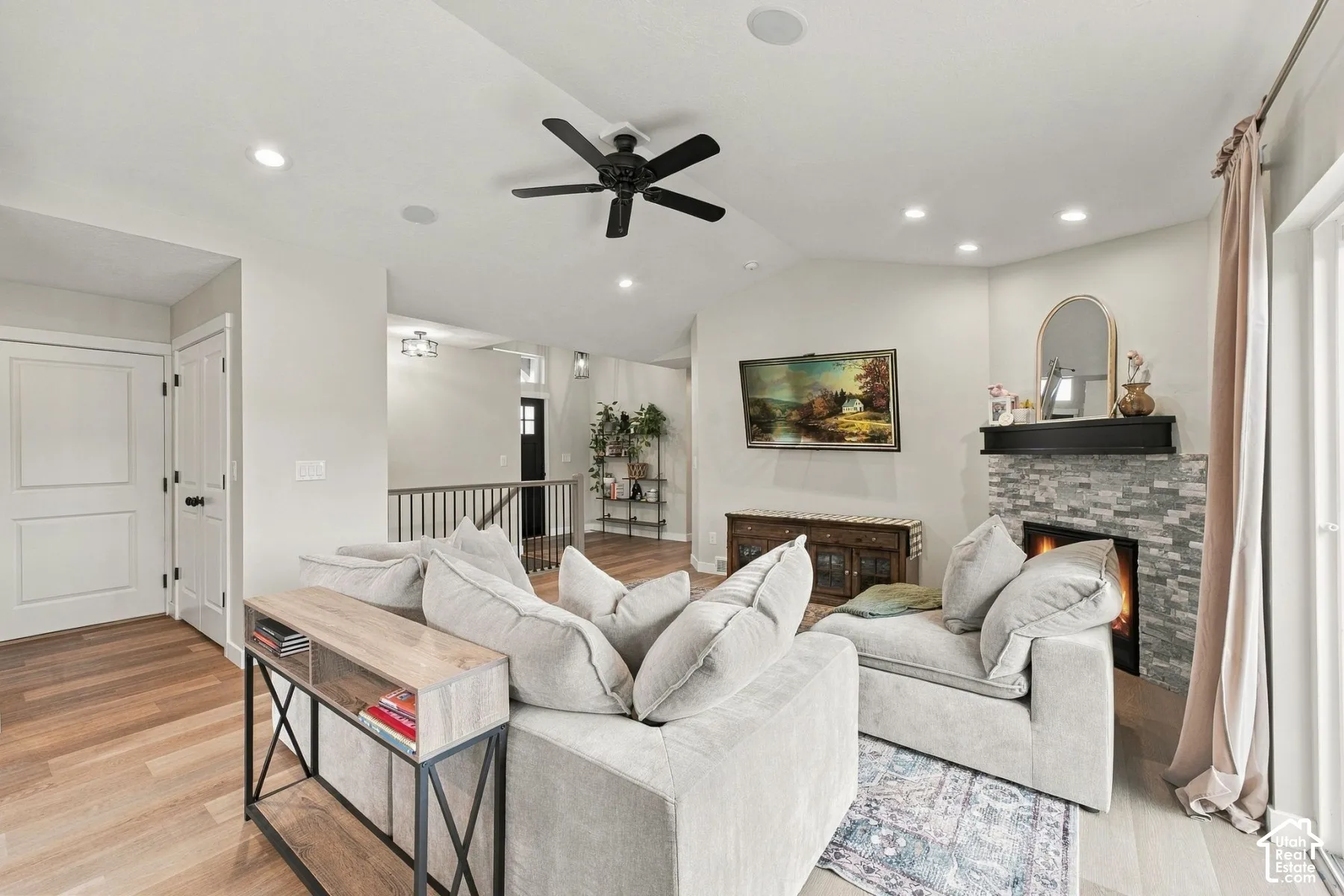Vaulted ceilings featuring recessed lighting and a matte black ceiling fan, stone-surround fireplace with a black mantel, and wood-finish flooring