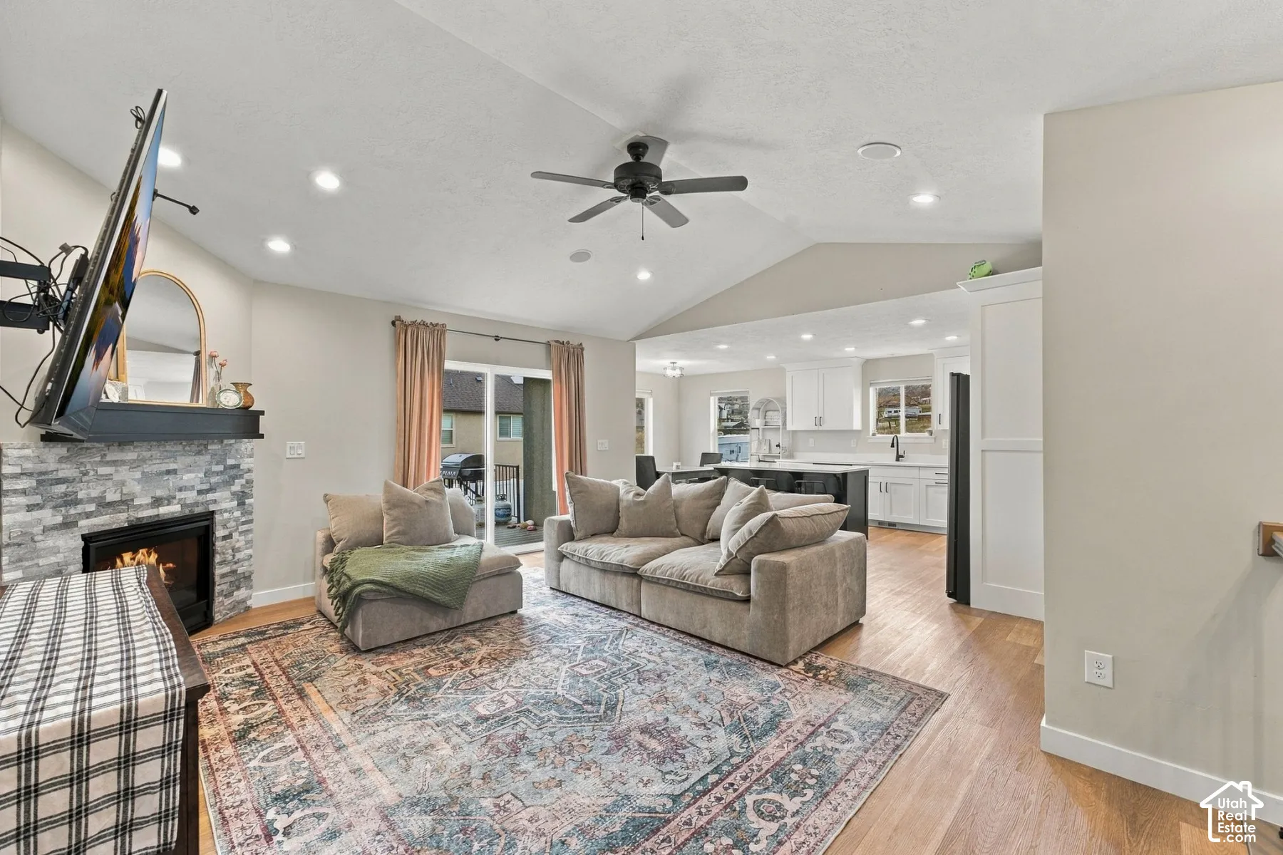 Vaulted ceilings with recessed lighting, stone-surround fireplace with a dark mantle, and wood-finish flooring