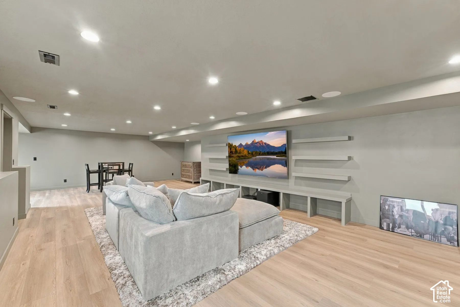Open-concept room featuring light wood-finish flooring, recessed lighting, built-in low-profile cabinetry, and tiered floating shelving