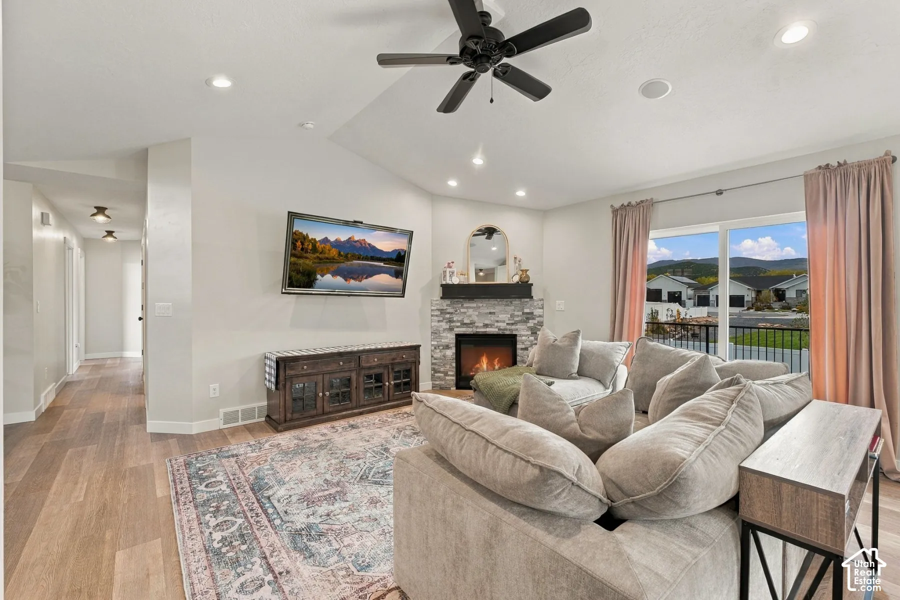 Vaulted ceiling with integrated recessed lighting, corner fireplace with stone veneer surround, and wood-finish flooring