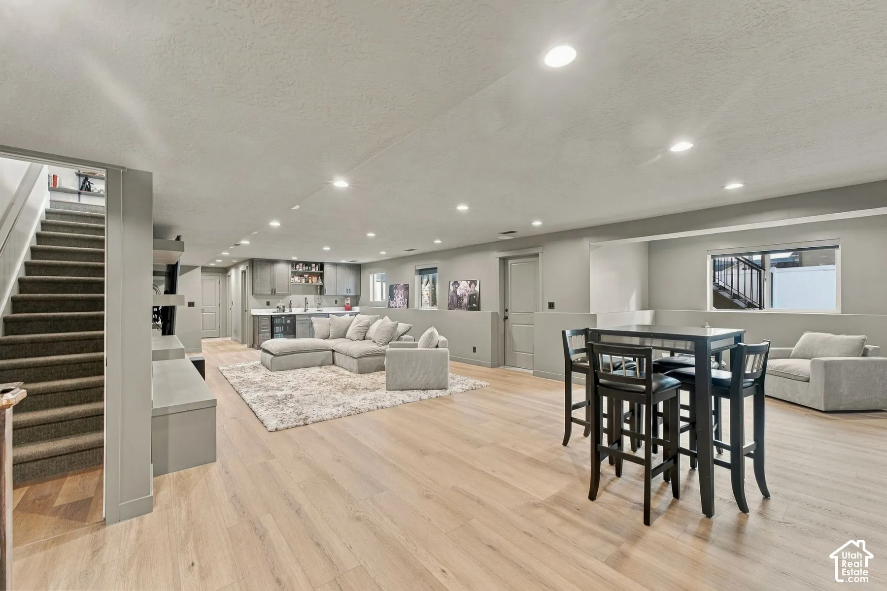 Open-concept interior featuring light wood-finish flooring, recessed lighting, a built-in wet bar with cabinetry, and carpeted stairs