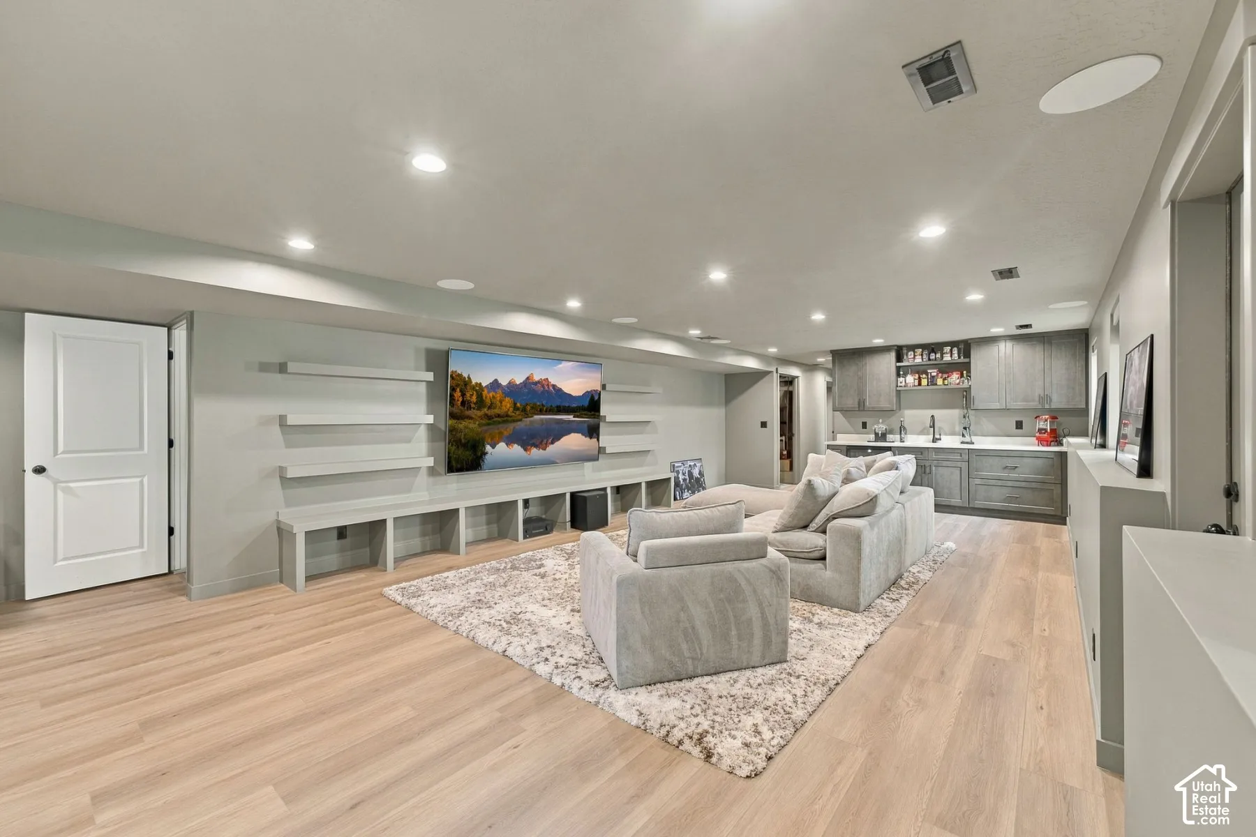 Open-concept room featuring wood-finish flooring, recessed lighting, built-in shelving and cabinetry, and a wet bar with stone countertops