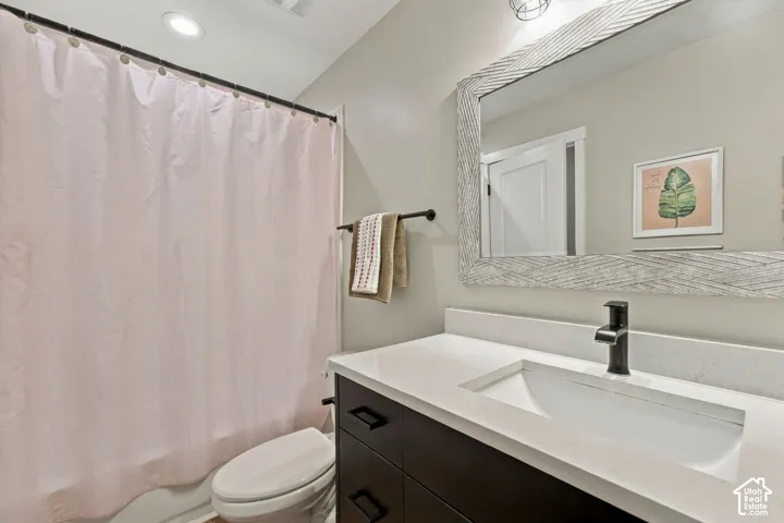 Bathroom vanity featuring a stone countertop, integrated basin, matte black faucet, and dark-finish cabinetry with linear hardware