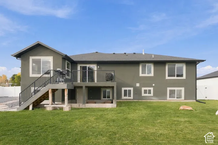 Rear exterior featuring a raised deck with metal railings, a staircase leading to the ground level, multi-pane windows, and an expansive grass lawn