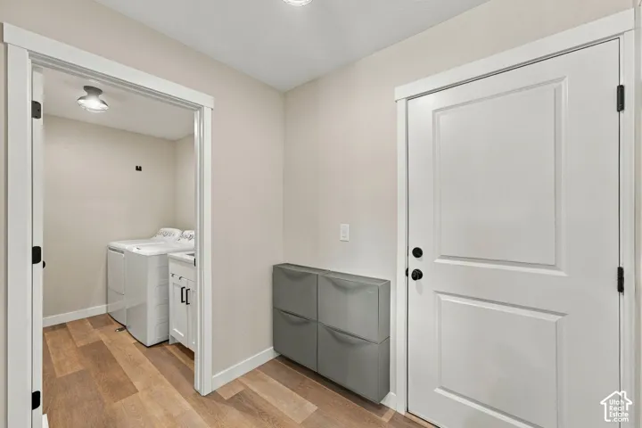 Utility room featuring wood-finish flooring, white cabinetry, and recessed lighting, paired with a mudroom area containing wall-mounted storage and a paneled entry door with matte black hardware