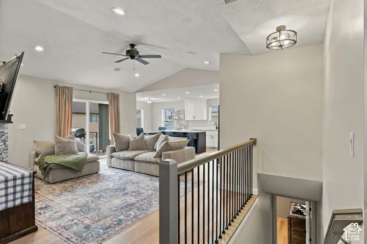 Vaulted ceilings, recessed lighting, matte black ceiling fan, wood-finish flooring, and black metal stair railing