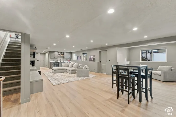 Open-concept interior featuring light wood-finish flooring, recessed lighting, a built-in wet bar with cabinetry, and carpeted stairs