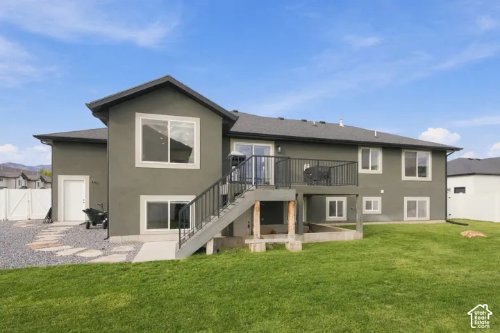 Stucco exterior featuring an elevated deck with metal railings, a stone-paved walkway, and a spacious grass yard