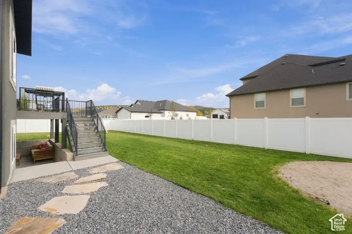 Fenced backyard featuring an elevated deck with metal railings, a stone-paved patio, and a grass lawn