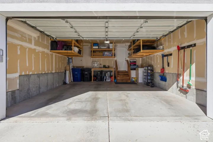 Two-car garage featuring a concrete floor, overhead sectional door, built-in wooden wall shelving, and a separate service door with steps