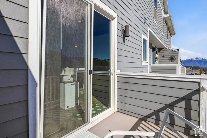 Exterior balcony featuring gray horizontal siding, a sliding glass door, wall-mounted exterior lighting, and mountain scenery