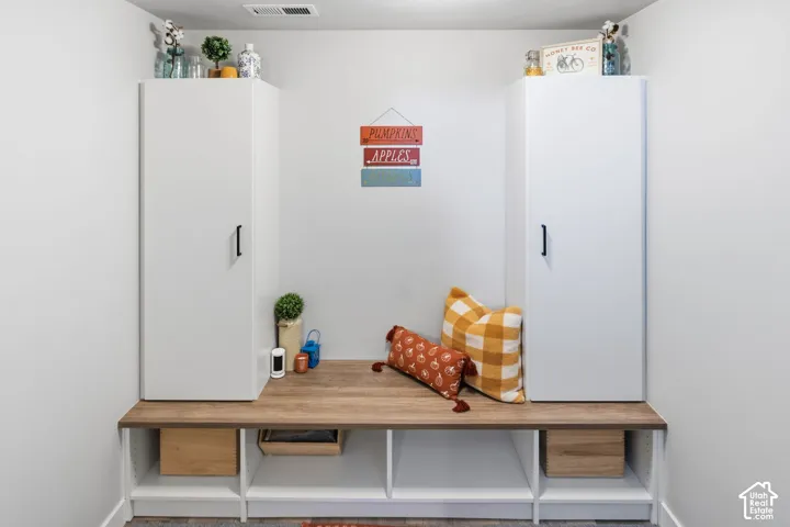 Base of basement stairs. Built-in floor-to-ceiling white cabinetry with matte black hardware, accompanied by a custom wood-finish bench featuring lower open shelving compartments