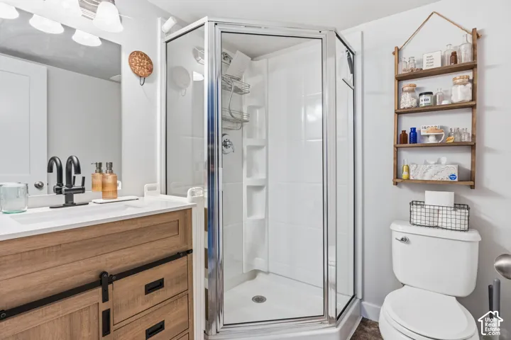 Basement bathroom featuring a wood-finish vanity with a rectangular sink, matte black faucet, and corner shower enclosure with a glass door