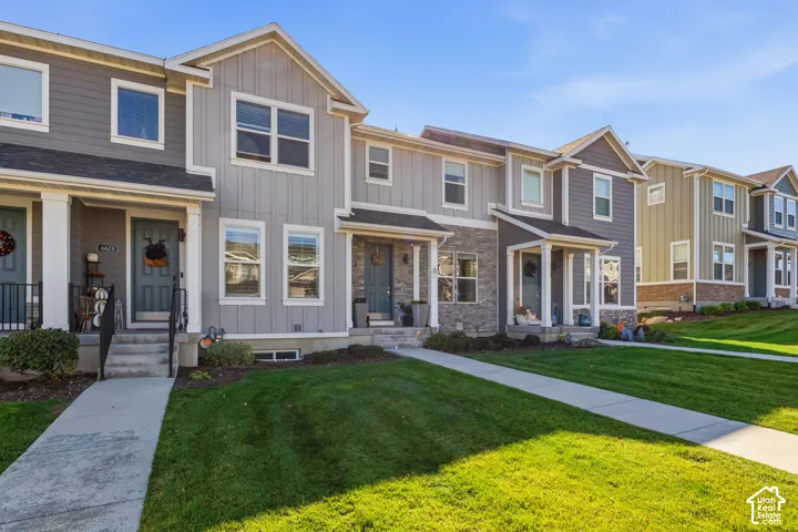 Multi-family exterior featuring vertical board-and-batten siding, stone veneer accents, covered entry porches, concrete walkways, and manicured lawn