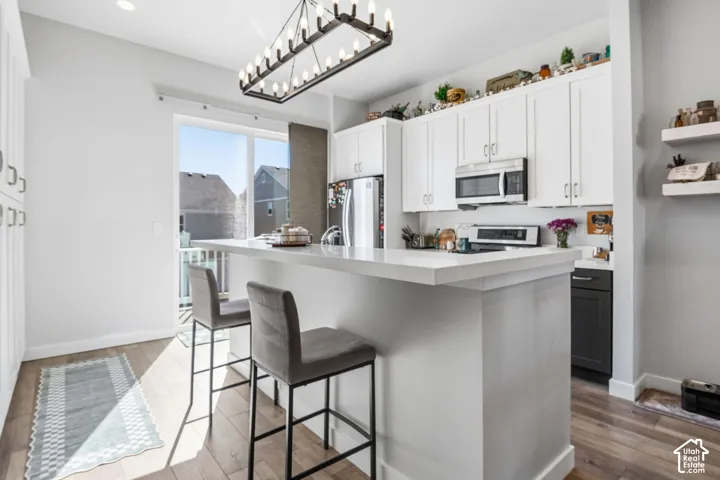 Kitchen featuring white cabinetry, quartz-surface island, wood-finish flooring, rectangular chandelier with candelabra-style bulbs, and stainless-steel appliances