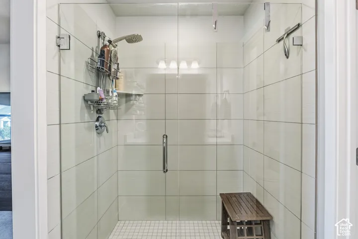 Walk-in shower featuring large-format ceramic wall tile, a frameless glass door, a built-in shelf, chrome fixtures, and a mosaic tile floor