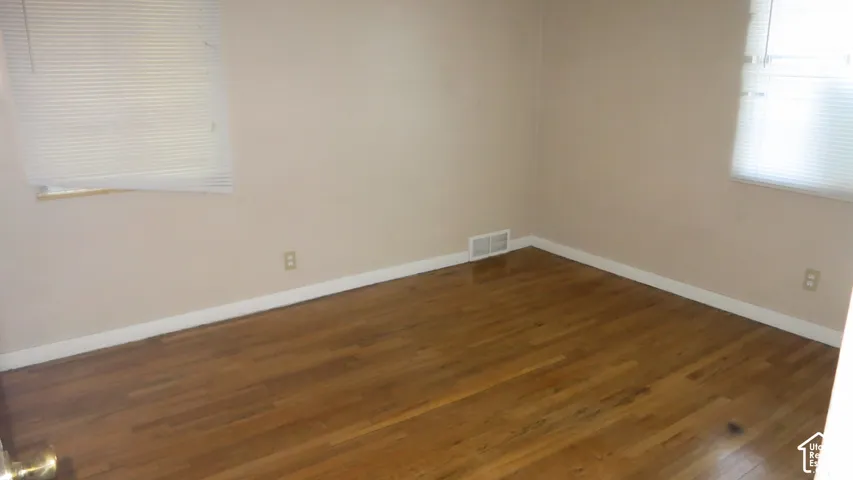 Room featuring wood-finish flooring and two windows with horizontal blinds