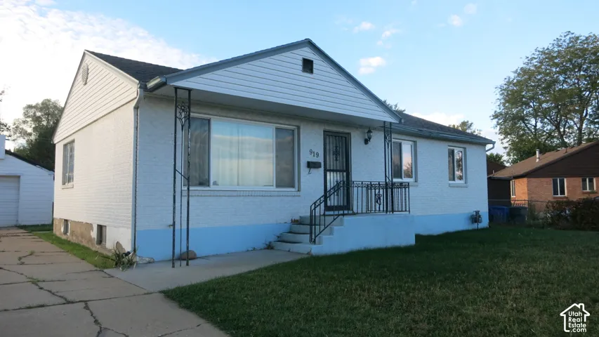 Single-story exterior featuring painted brick masonry, horizontal siding gable, concrete porch steps, decorative metal railing, and a concrete driveway