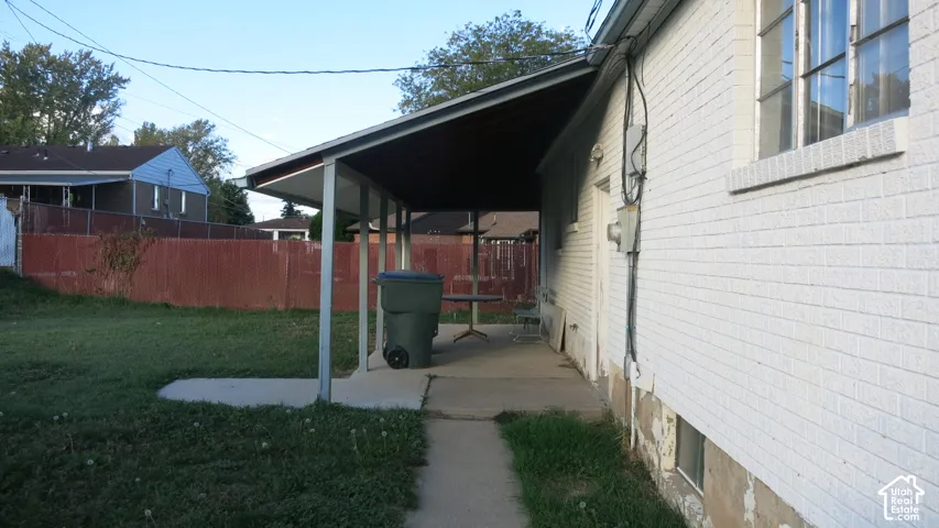 Exterior view of a white brick home featuring a covered patio, concrete walkway, and expansive lawn