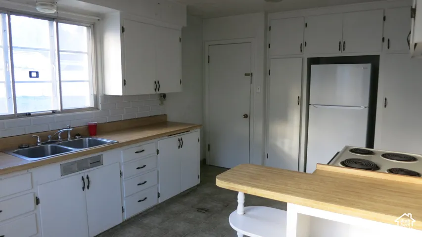 Kitchen featuring white cabinetry, light-toned laminate countertops, a double-basin stainless steel sink, tiled backsplash, and built-in appliances