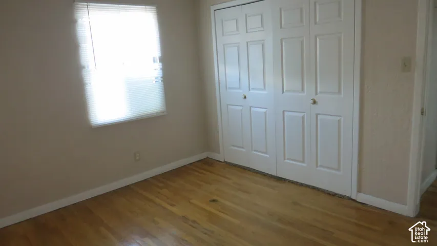 Room featuring wood-finish flooring, a single window, and a white paneled bi-fold closet door