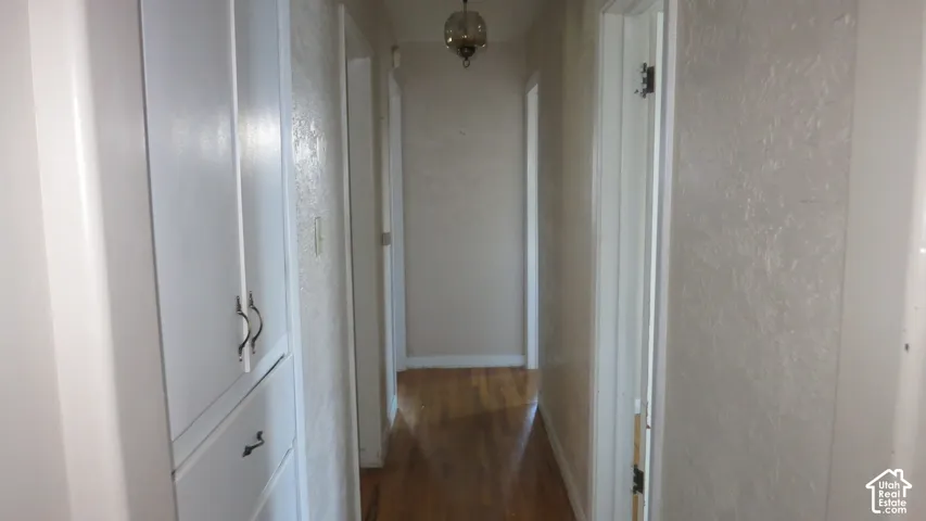 Hallway featuring wood-finish flooring, built-in white cabinetry, textured walls, and a decorative glass pendant light fixture