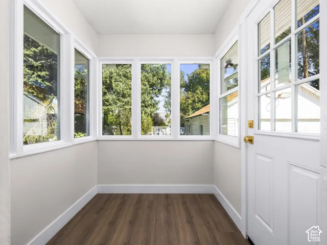 Sunroom featuring wood-finish flooring, white wall trim, and a multi-pane glass entry door surrounded by windows with white frames