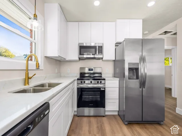 Kitchen featuring white shaker-style cabinetry, stone-surface countertops, wood-finish flooring, a brass-tone gooseneck faucet, and stainless steel appliances