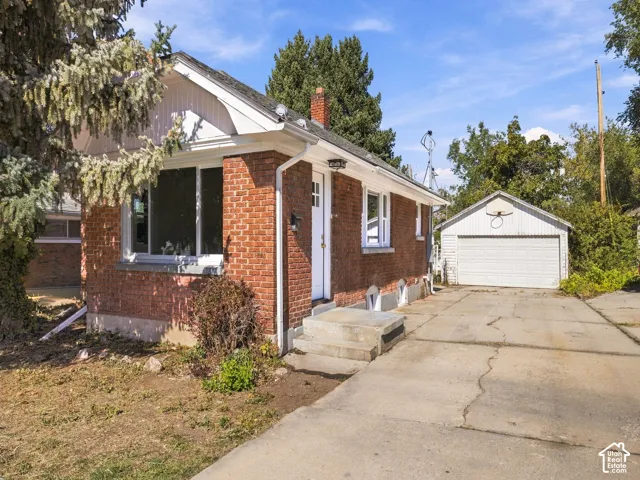 Red brick exterior with white trim, gable roofline, concrete driveway, and detached garage