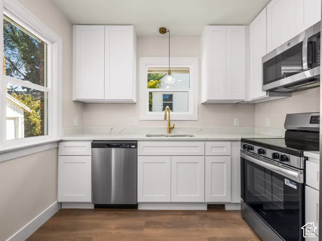 Kitchen featuring white shaker-style cabinetry, stone-surface countertops, wood-finish flooring, stainless steel appliances, and a brass-tone gooseneck faucet