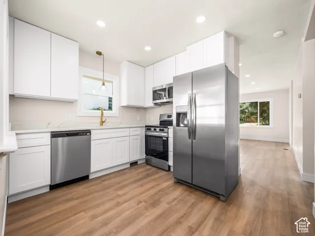 Kitchen featuring white shaker-style cabinetry, stainless steel appliances, stone-patterned countertops, a gold-tone faucet, and wood-finish flooring
