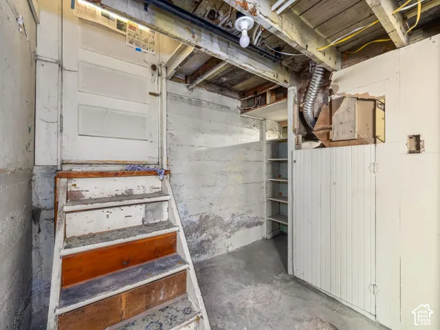 Unfinished lower-level storage area featuring concrete foundation walls, built-in shelving, wooden staircase, and beadboard wall paneling
